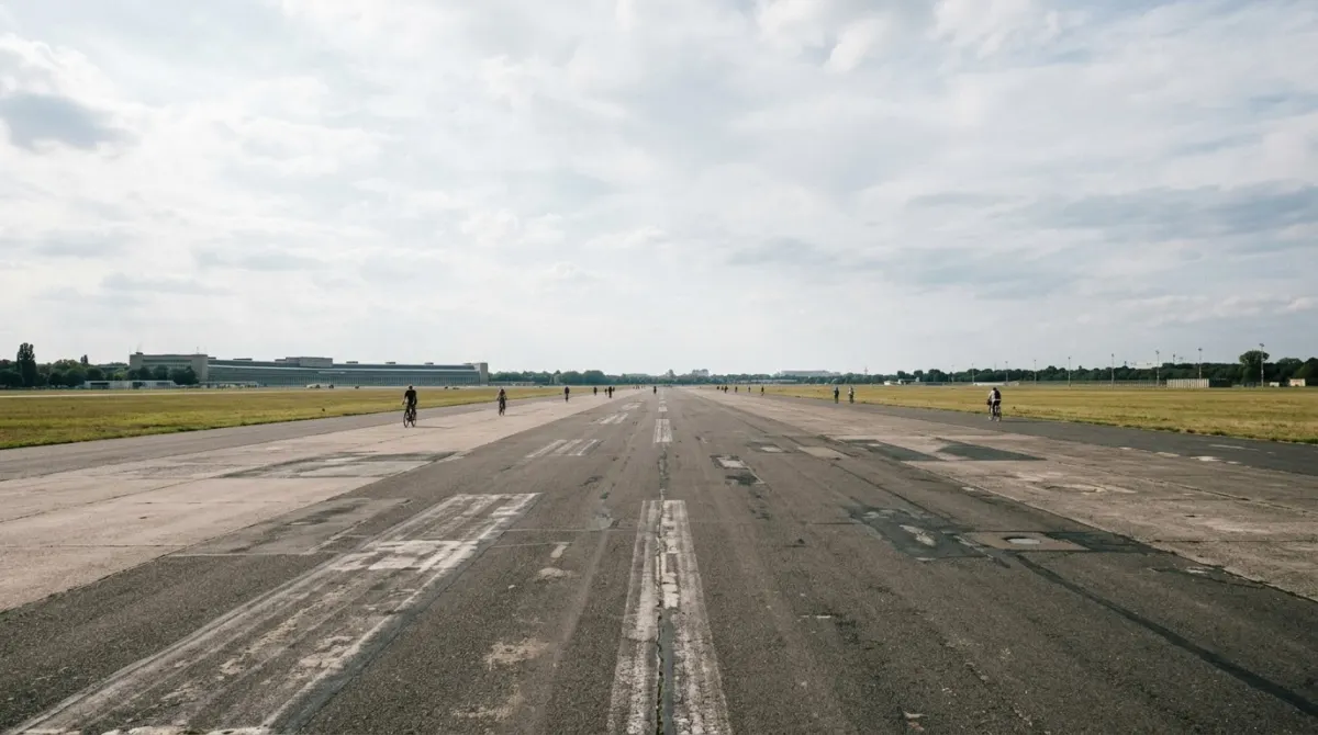 Cyclists small in the distance on a wide former airport runway under a big open sky, Tempelhofer Feld, Berlin, Germany