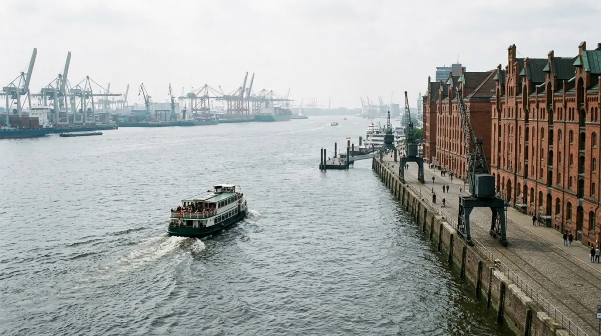 Brick warehouses and cranes along a wide harbour with a ferry crossing the water, Hamburg, Germany