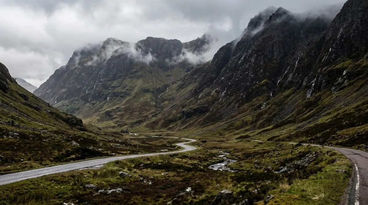 A narrow glen with steep dark mountain flanks and a winding road under low cloud, Glencoe, Scotland