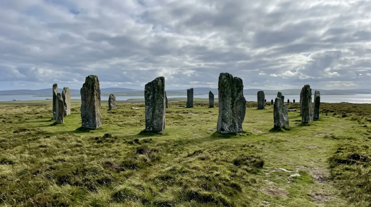 Tall ancient standing stones in a ring on a green headland under a wide sky, Orkney, Scotland