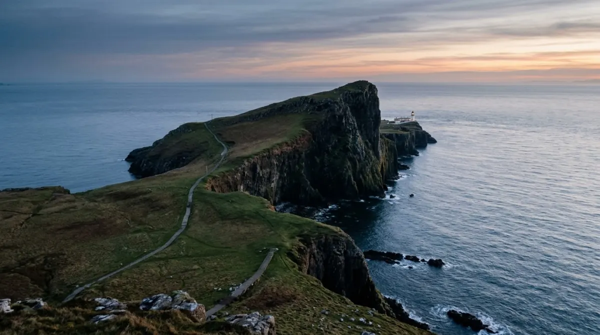 A white lighthouse at the end of steep sea cliffs above a calm sea at dusk, Neist Point, Skye, Scotland