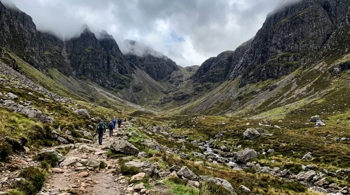 Walkers small on a rocky path into a hidden corrie between steep mountain walls, Lost Valley, Glencoe, Scotland