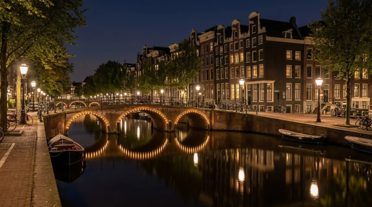 Lit arched bridges reflected in a still canal at night with tall houses along the bank, Prinsengracht, Amsterdam, Netherlands