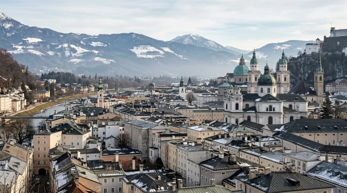 Baroque church domes and old town roofs with snowy alpine peaks rising on the horizon, Salzburg, Austria
