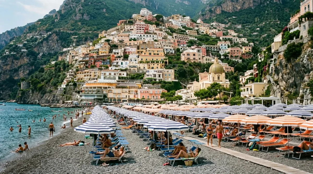 Rows of striped sunbeds and umbrellas on a grey pebble beach below the stacked village, Spiaggia Grande, Positano, Italy