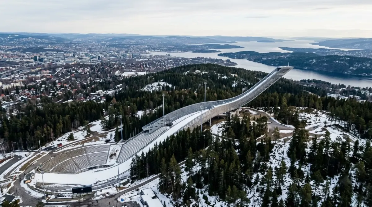 A sweeping modern ski jump ramp on a forested hilltop with the city and fjord far below, Holmenkollen, Oslo, Norway