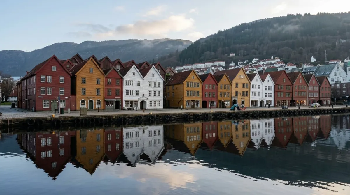 A row of colourful wooden wharf houses with pointed gables reflected in a still harbour early in the morning, Bryggen, Bergen, Norway