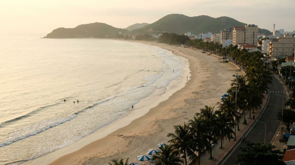 Illustration of Vung Tau Back Beach at sunrise with palm trees and seafront buildings, for a guide to the best hotels in Vung Tau